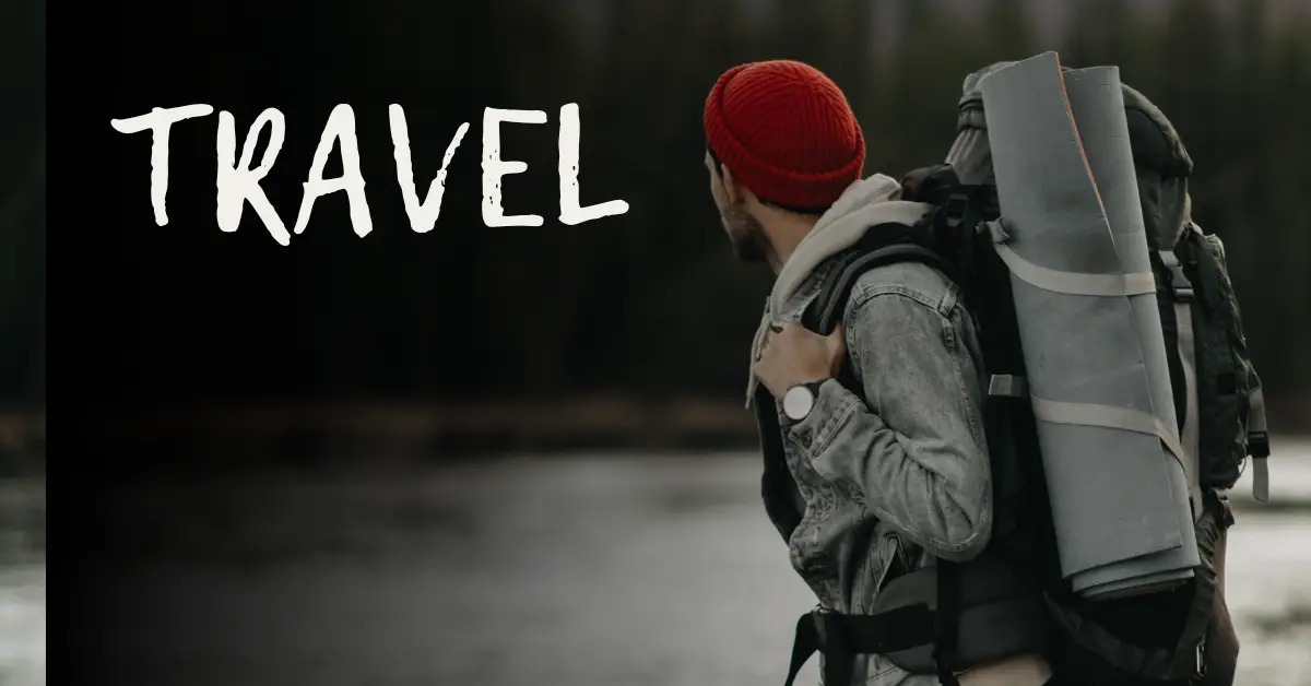 A man wearing a red hat and carrying a backpack stands by a serene lake, enjoying the tranquil scenery.