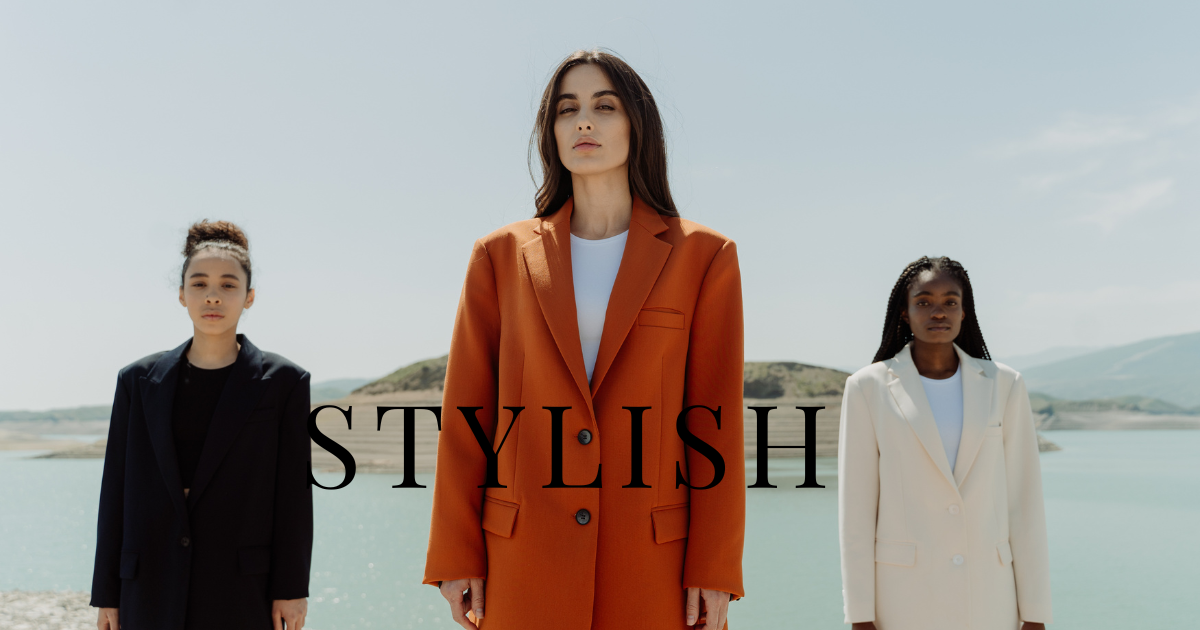 Three women in professional suits stand beside a serene body of water, exuding confidence and camaraderie.